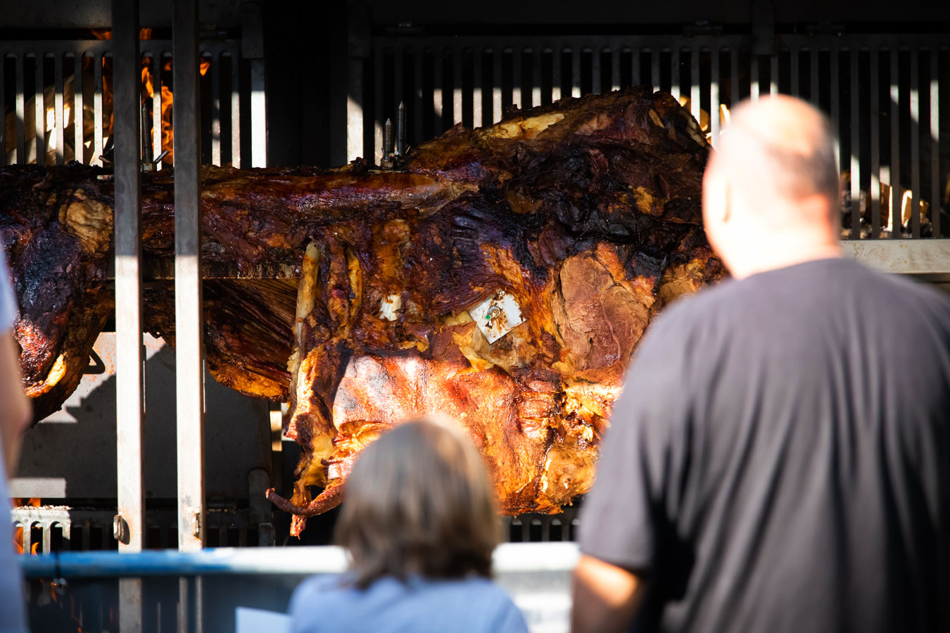 Zwei Menschen schauen auf einen 400kg Ochsen, der in einem großen Grill über Buchenholzfeuer zubereitet wird
